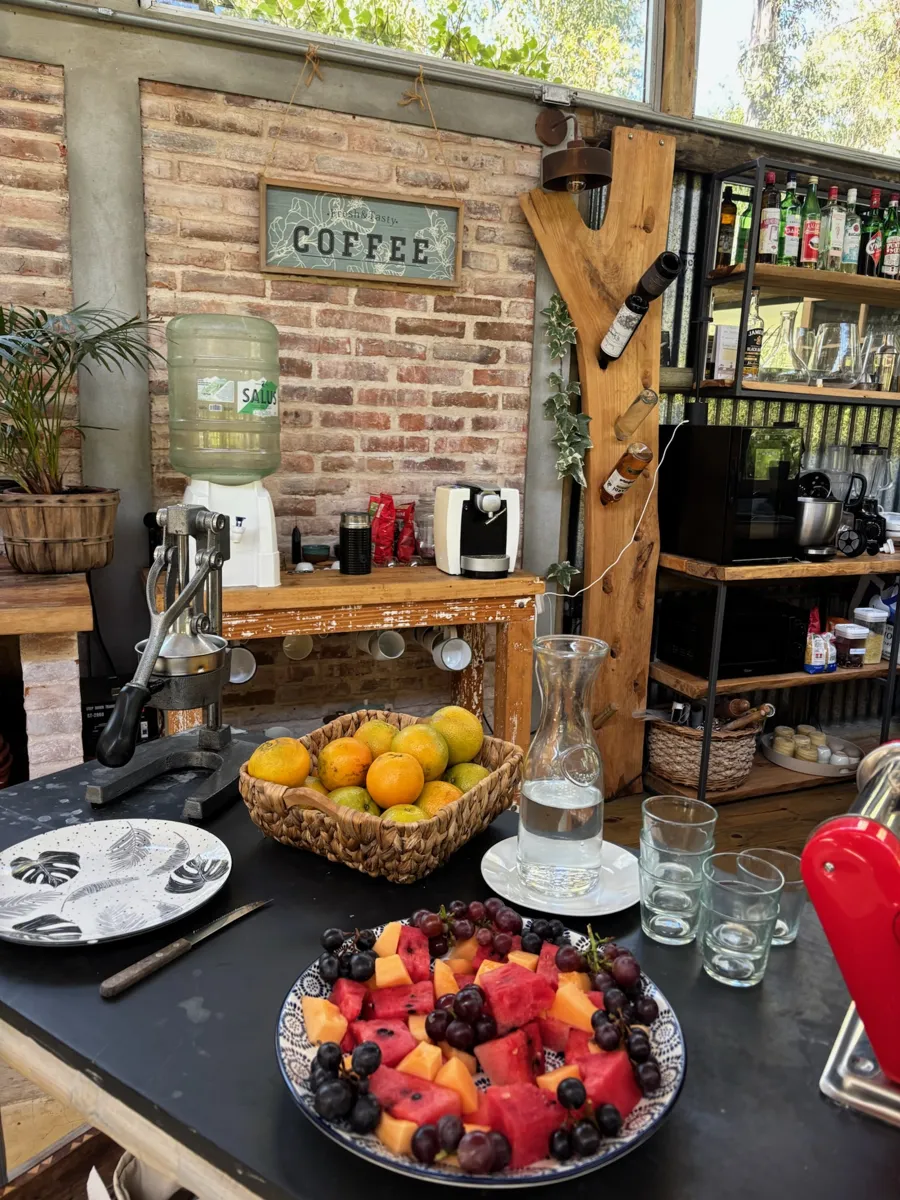 Mesa con frutas frescas, jarra de agua y rincón de café